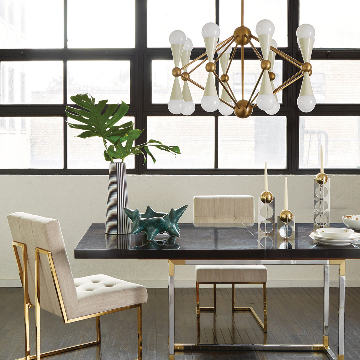 Hourglass-shaped lighting fixture over black dining table with plant and sculptural accents