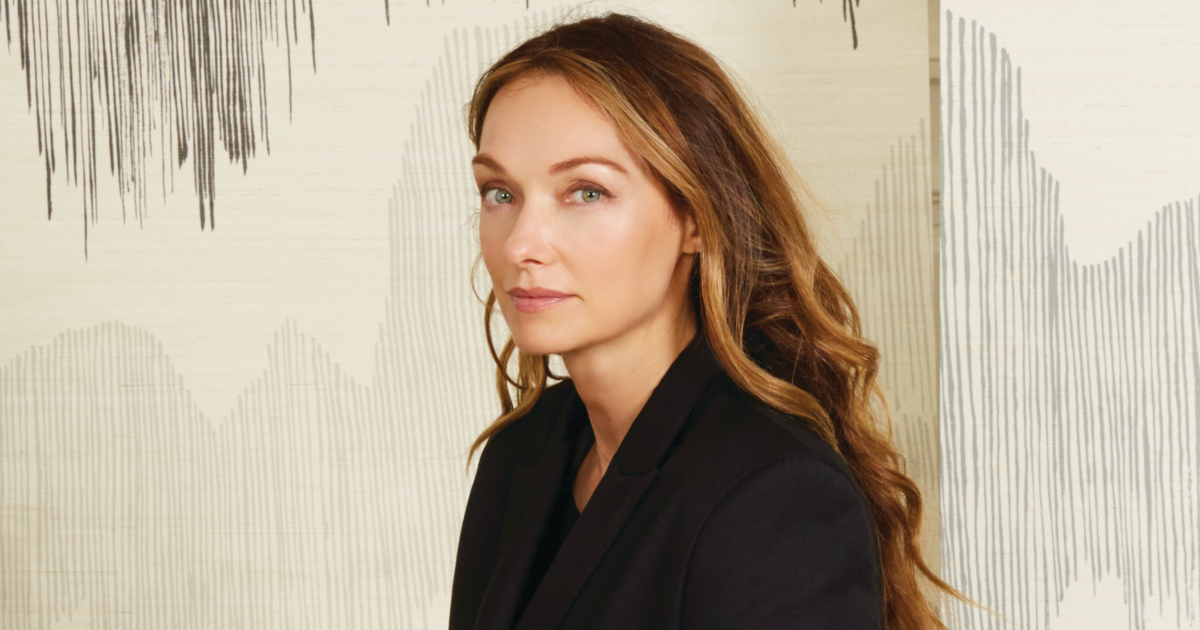 Headshot of designer Kelly Wearstler in black blazer on wavy-lined neutral background 