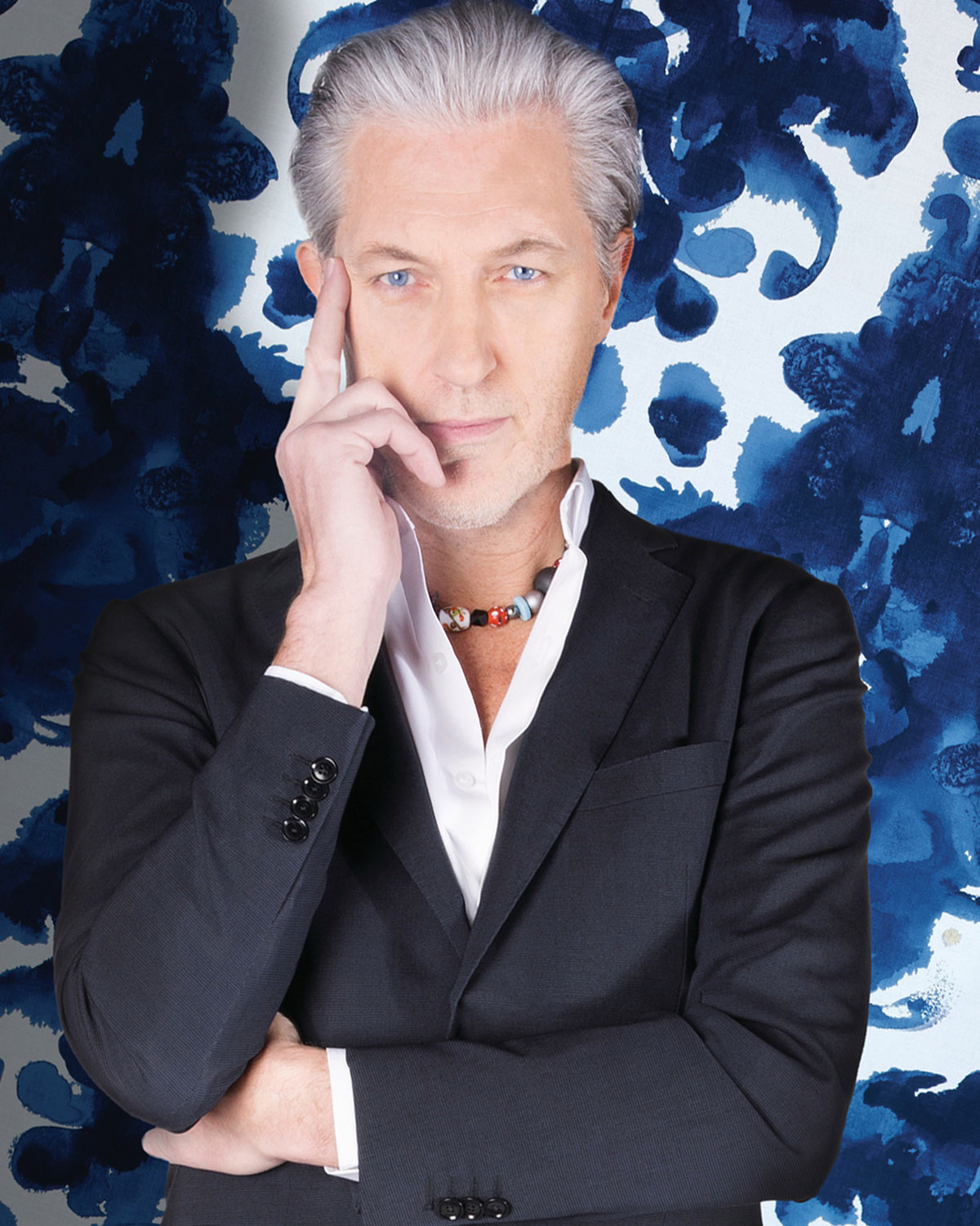 Marcel Wanders in black suit coat with beaded necklace on a blue painted background