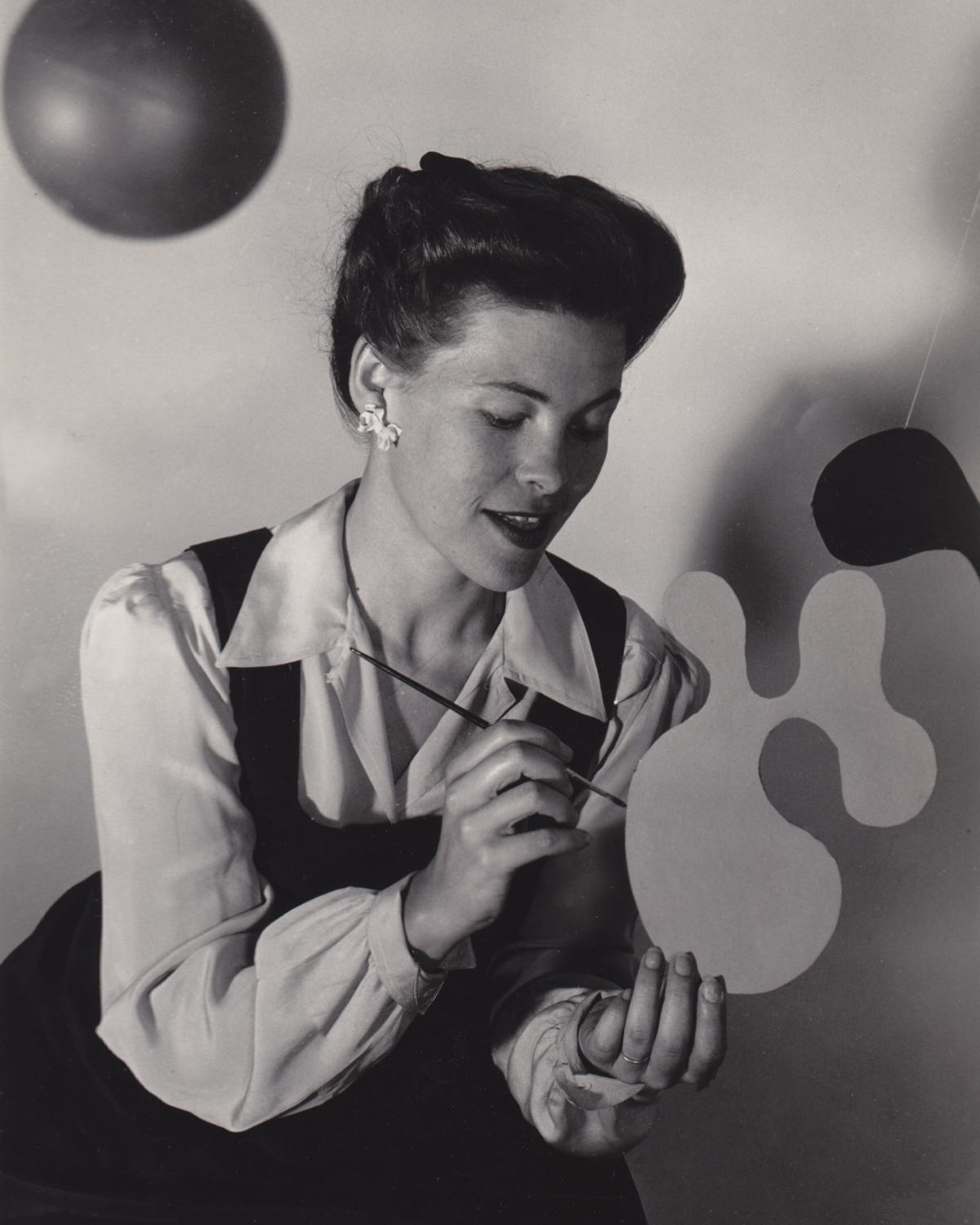 Black and white image of Ray Eames painting an abstract object
