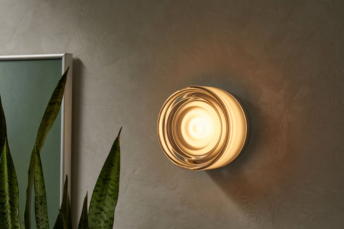 Circular wall sconce against a beige concrete wall with plant in foreground