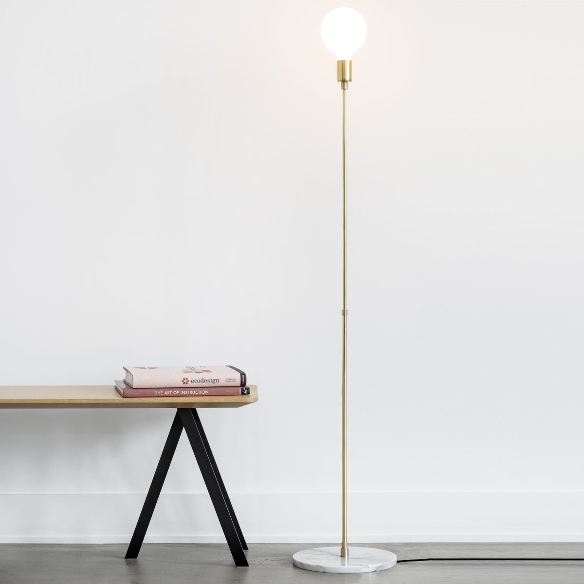 Tall golden lamp pole with lit bulb on top next to a wooden bench