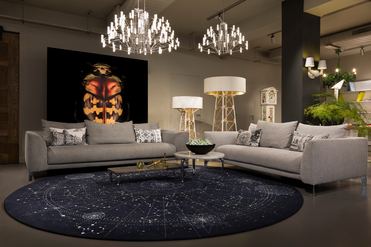 Two chandeliers over gray couches with constellation-covered blue rug