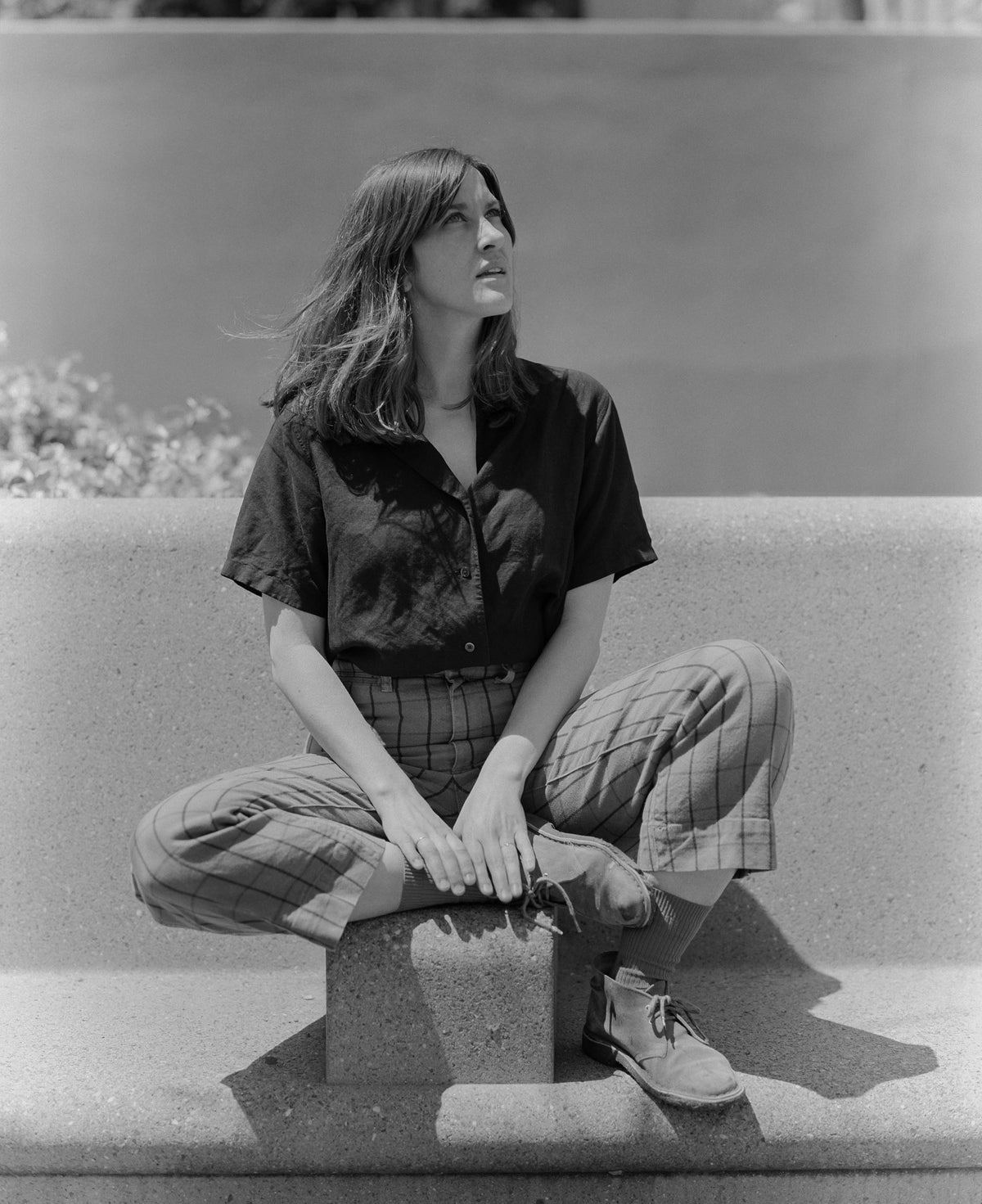 Woman in black shirt and plaid pants looking up towards the sky.