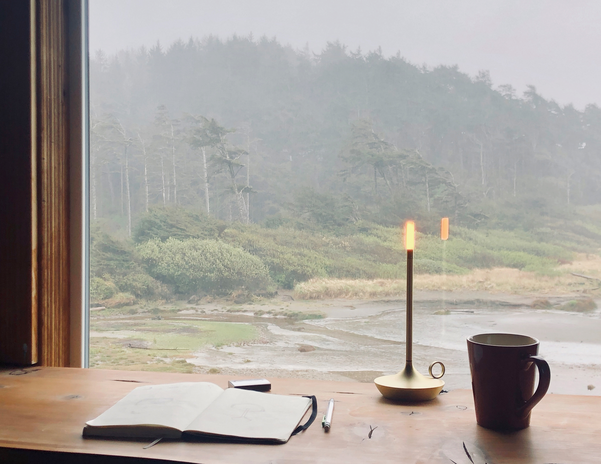 Candlestick-style light on rustic desk looking out on a natural forest landscape with mist.