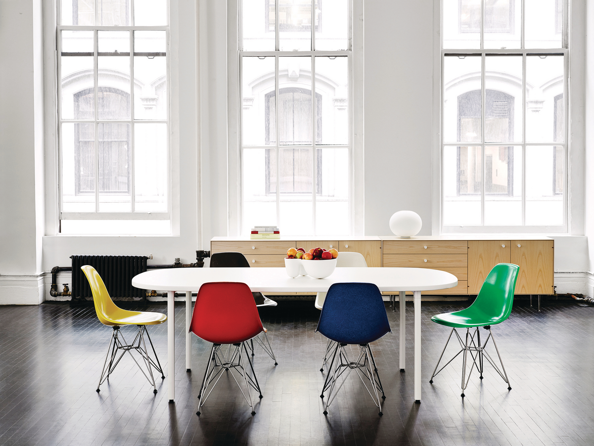 Multi-colored chairs around a white conference table in a white room with floor to ceiling windows