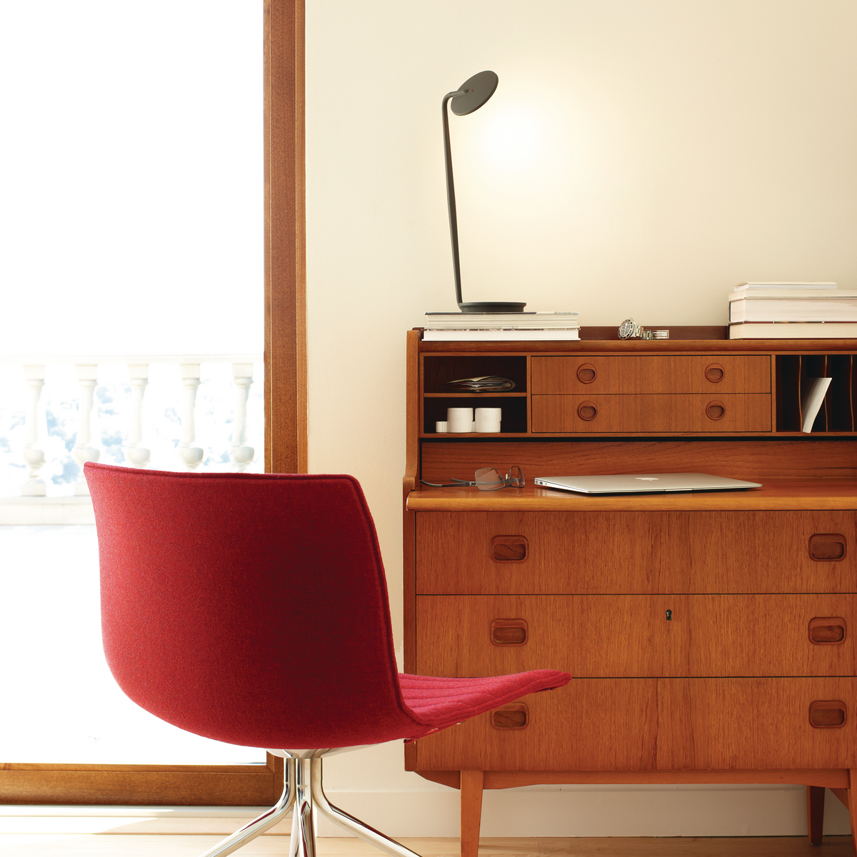 Red chair with natural wood desk and small black light.