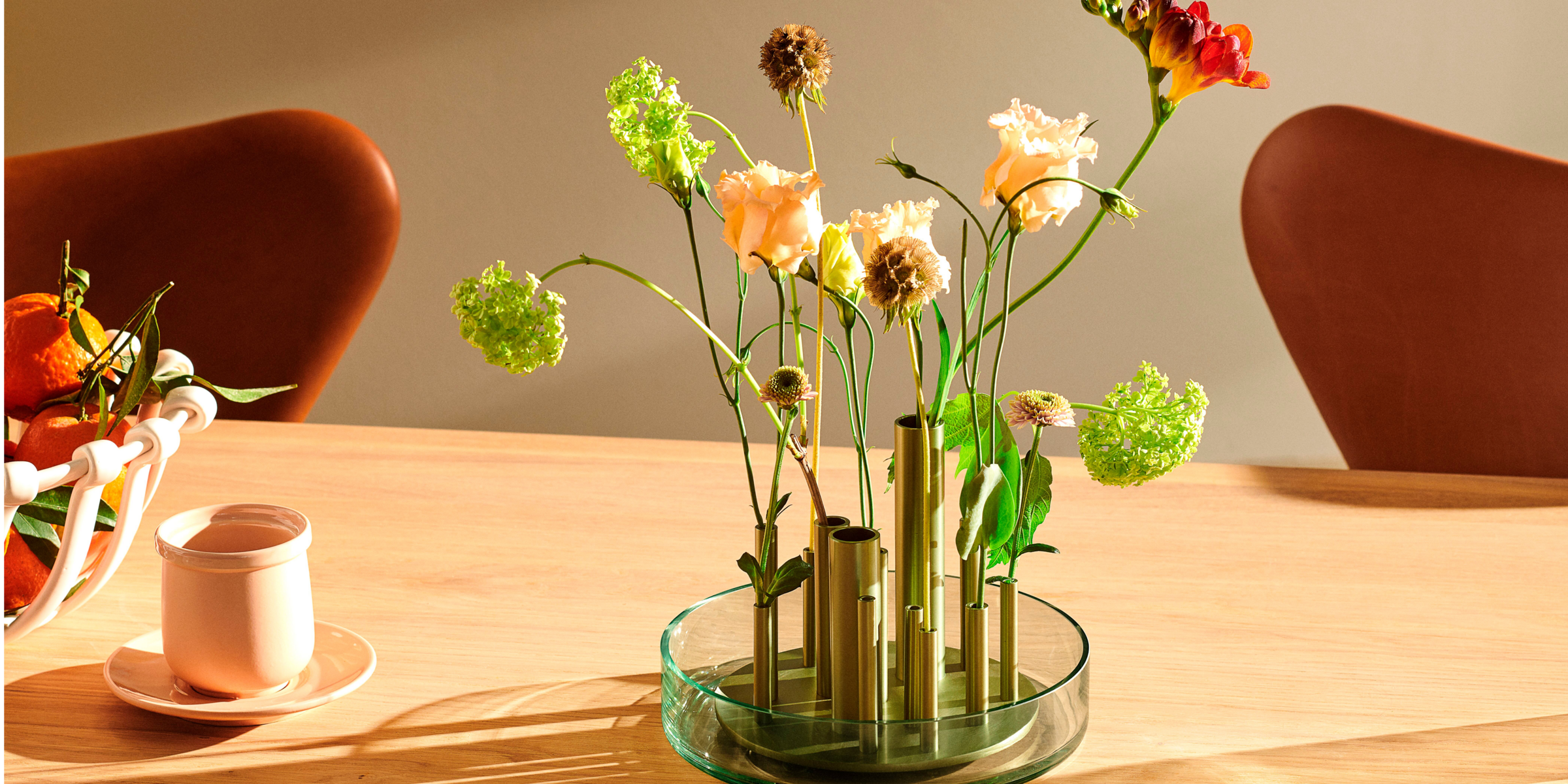 Unique flower vase with green hued metal tubes sitting inside a low glass bowl. 