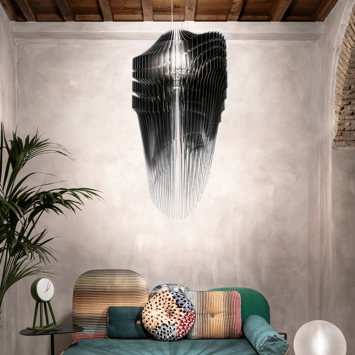 Oversized black, grey, and white pendant above green couch with colorful throw pillows