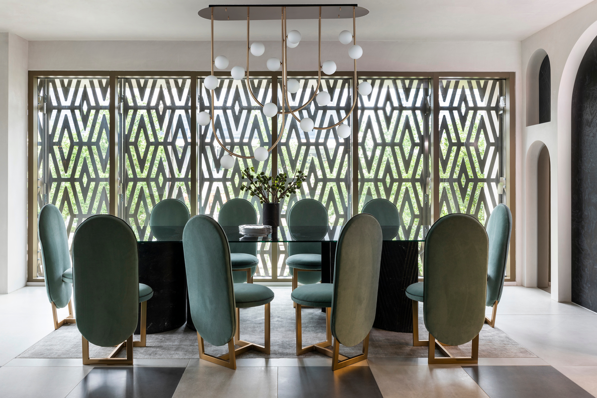 Curving pendant light over glass dining table with high-back green dining chairs