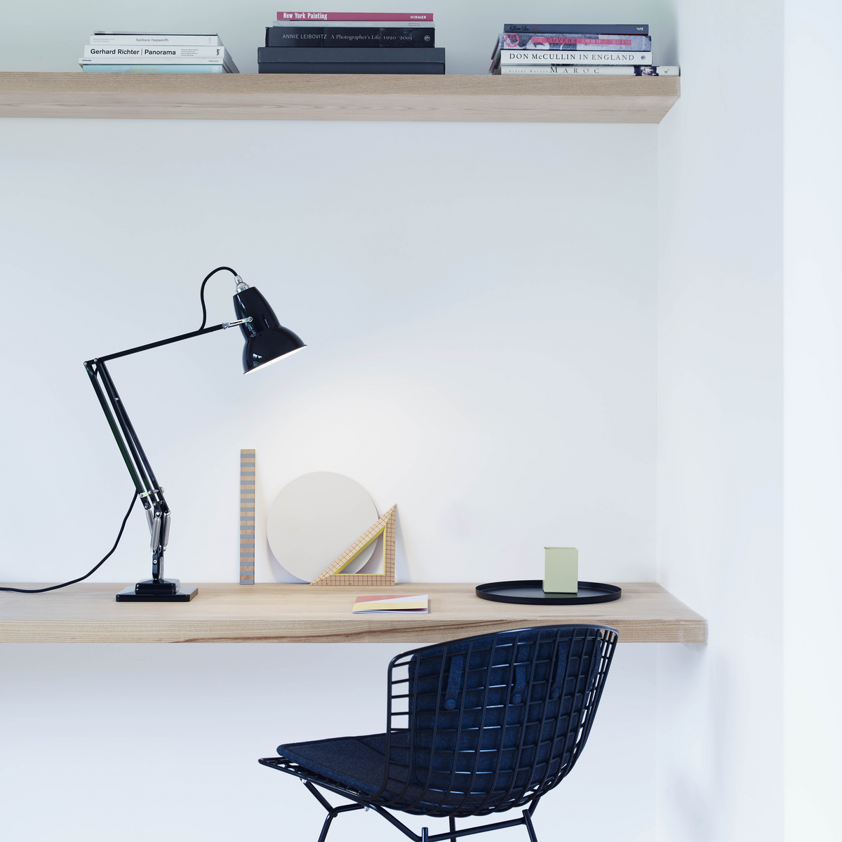 Black desk lamp on natural wood desk with wood shelf above