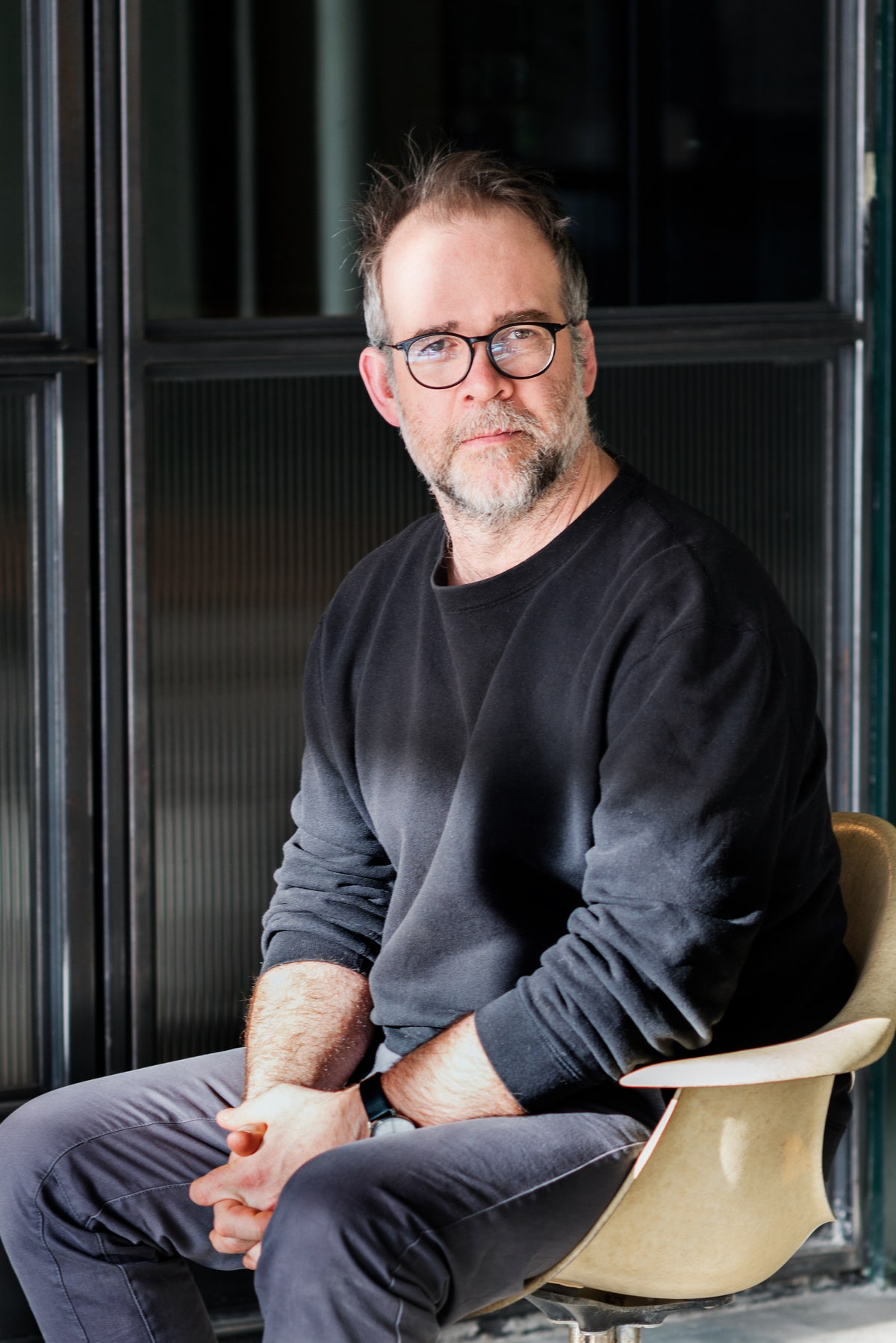 Man with gray beard, black glasses, wearing a black sweatshirt sitting in a chair