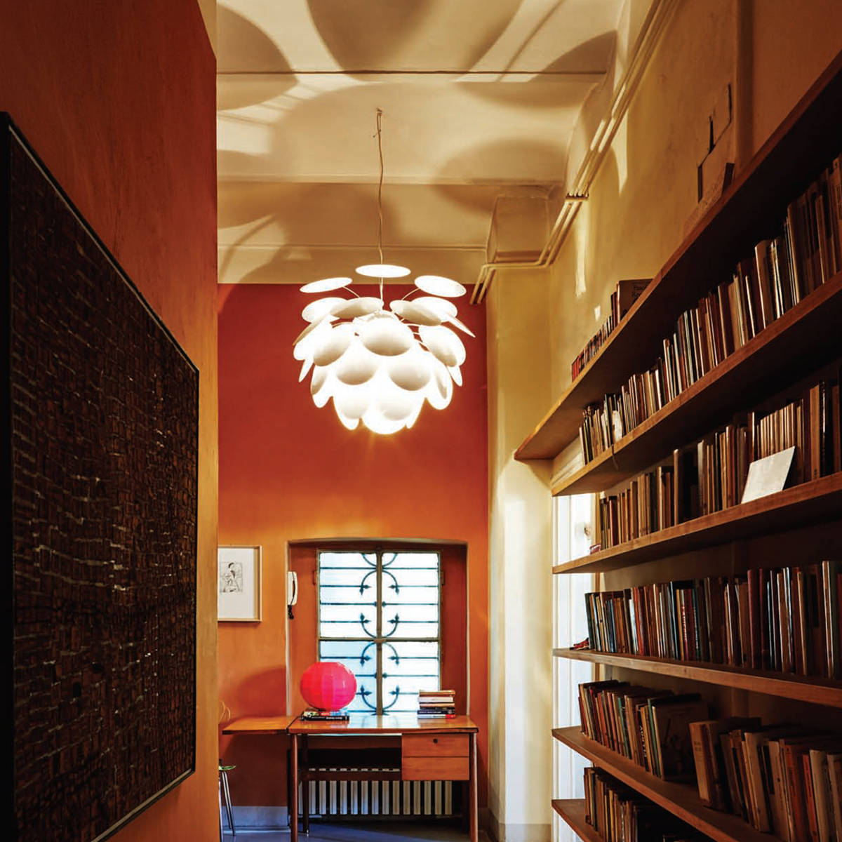 Glowing white pendant light leaves in a library-style hallway