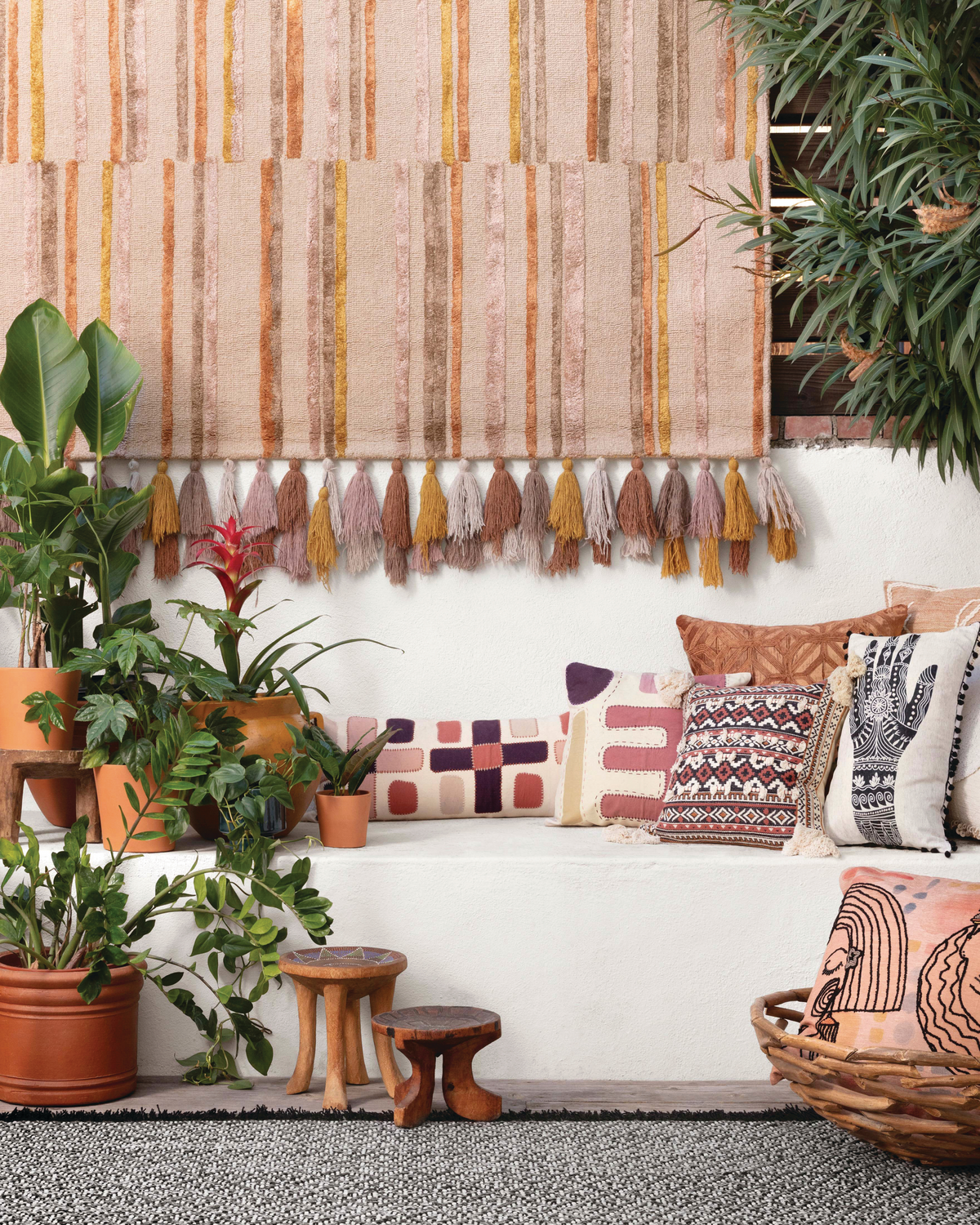 Terracotta, pink and cream patterned throw pillows on white concrete sofa area with plants