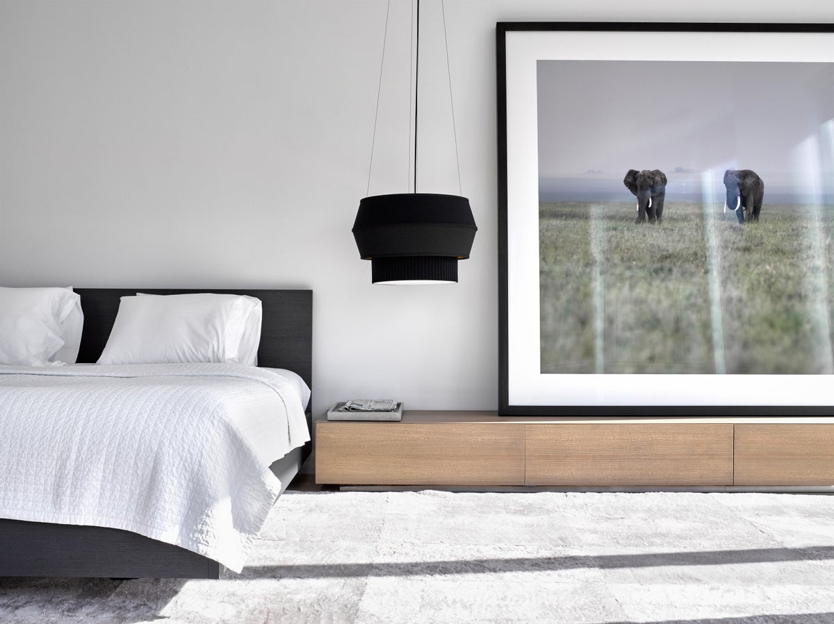 Black pendant light hanging next to a bed with a photograph of elephants in the background