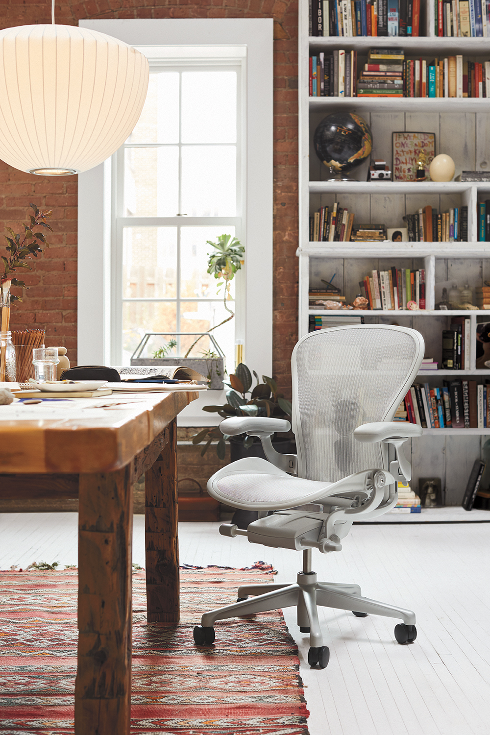 Vintage looking office with exposed brick wall, bookcase, and white pendant light