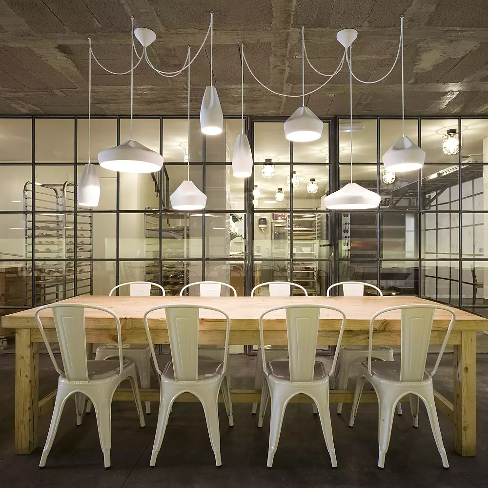 White pendant lighting hangs over an extended wood dining table with white chairs