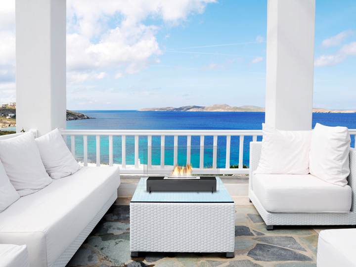 White outdoor upholstered furniture with fireplace against blue sea