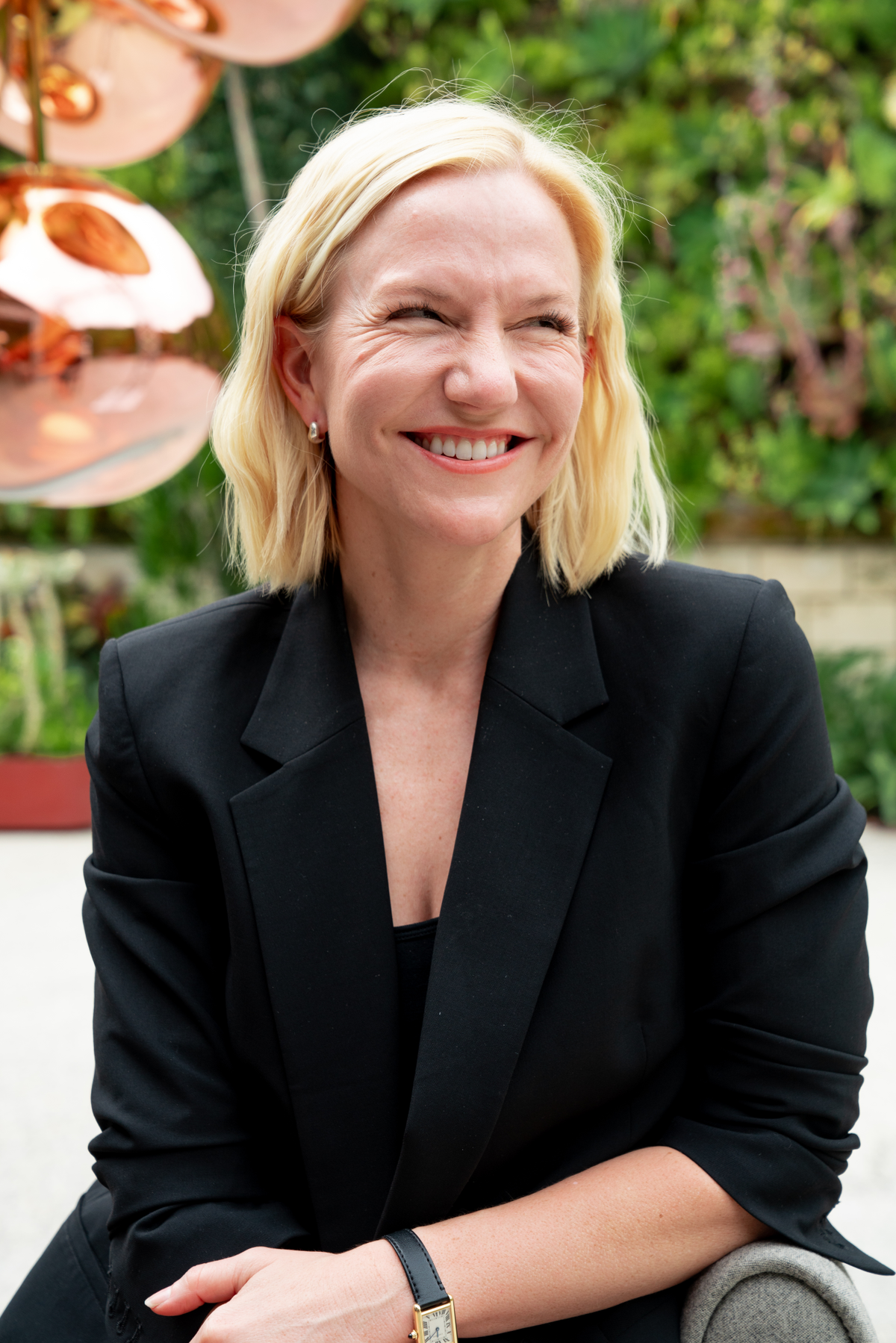 Blonde woman in a black blazer against a blurred green background