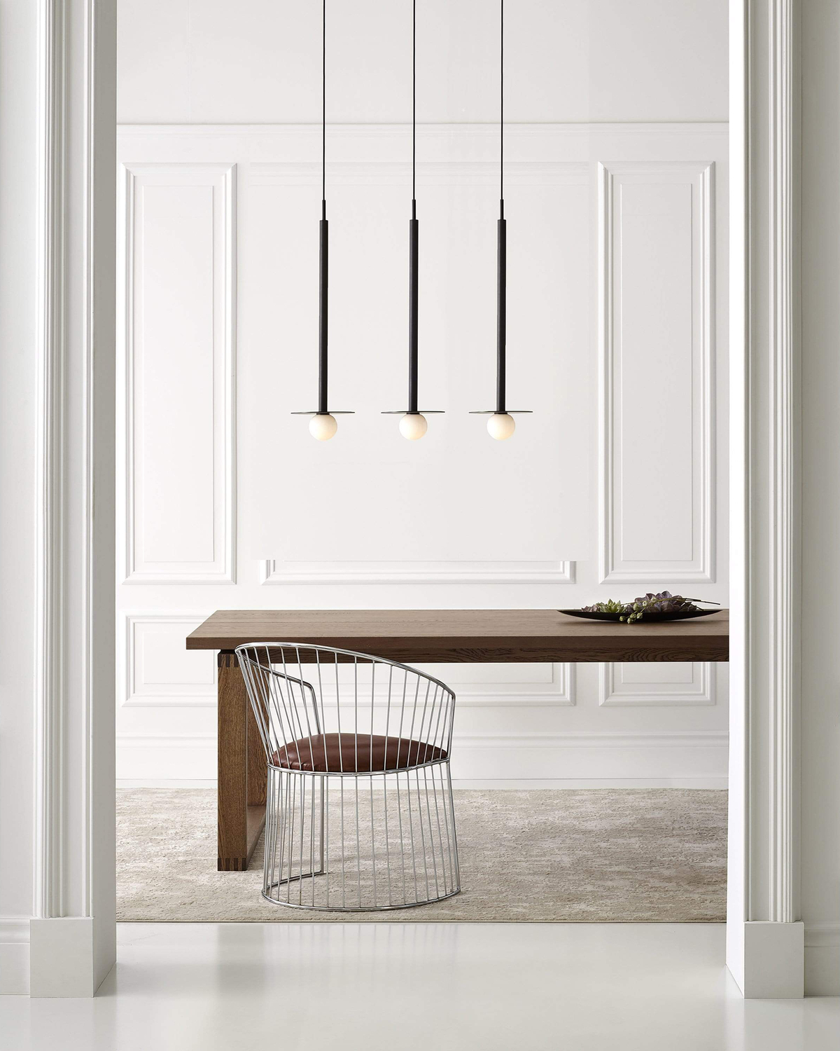 Three black pendant lights above wooden dining table in white dining room with chair