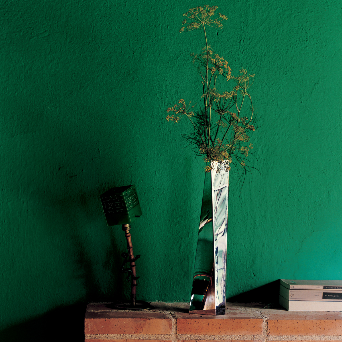 Metal flower vase on brick wall against green backdrop