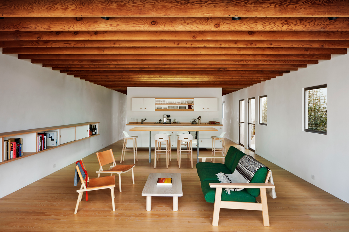 Minimalist interior space with green couch, white chairs and exposed rafters