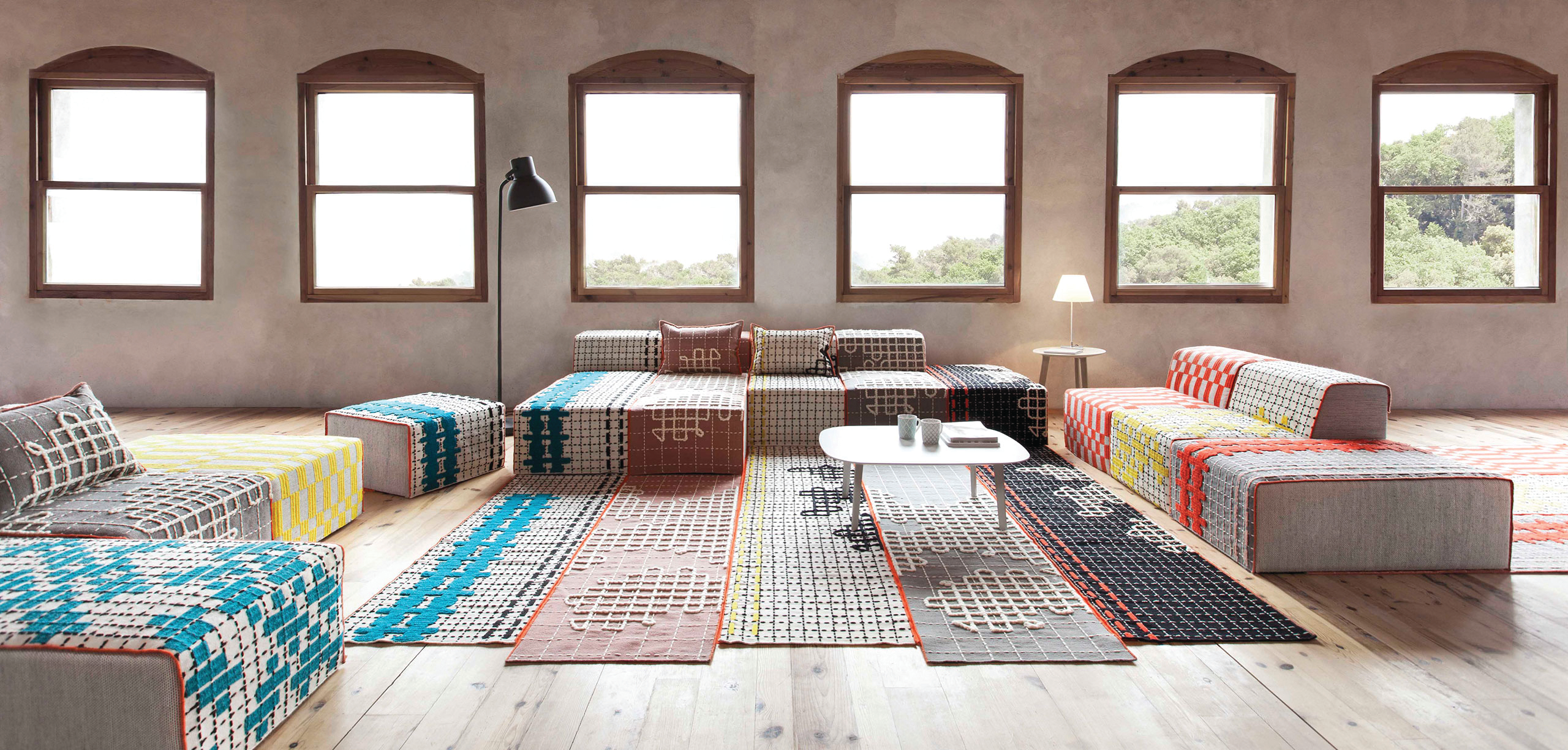 Multicolored rugs in a living space complete with furniture and coffee table with 6 windows in the background