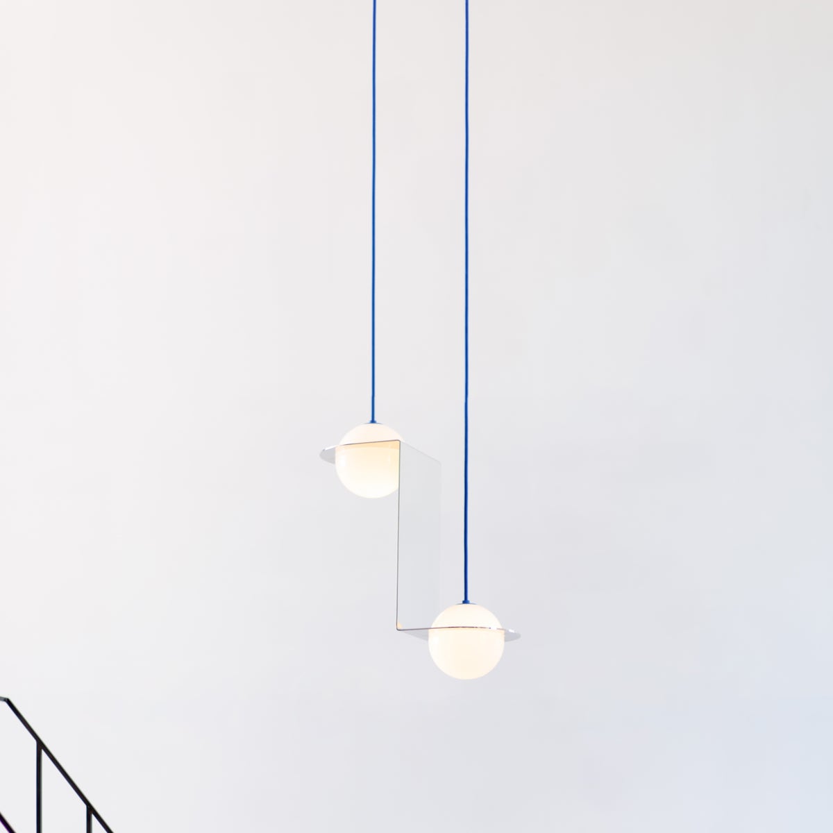 Two spherical lights hanging from blue cord against a white background