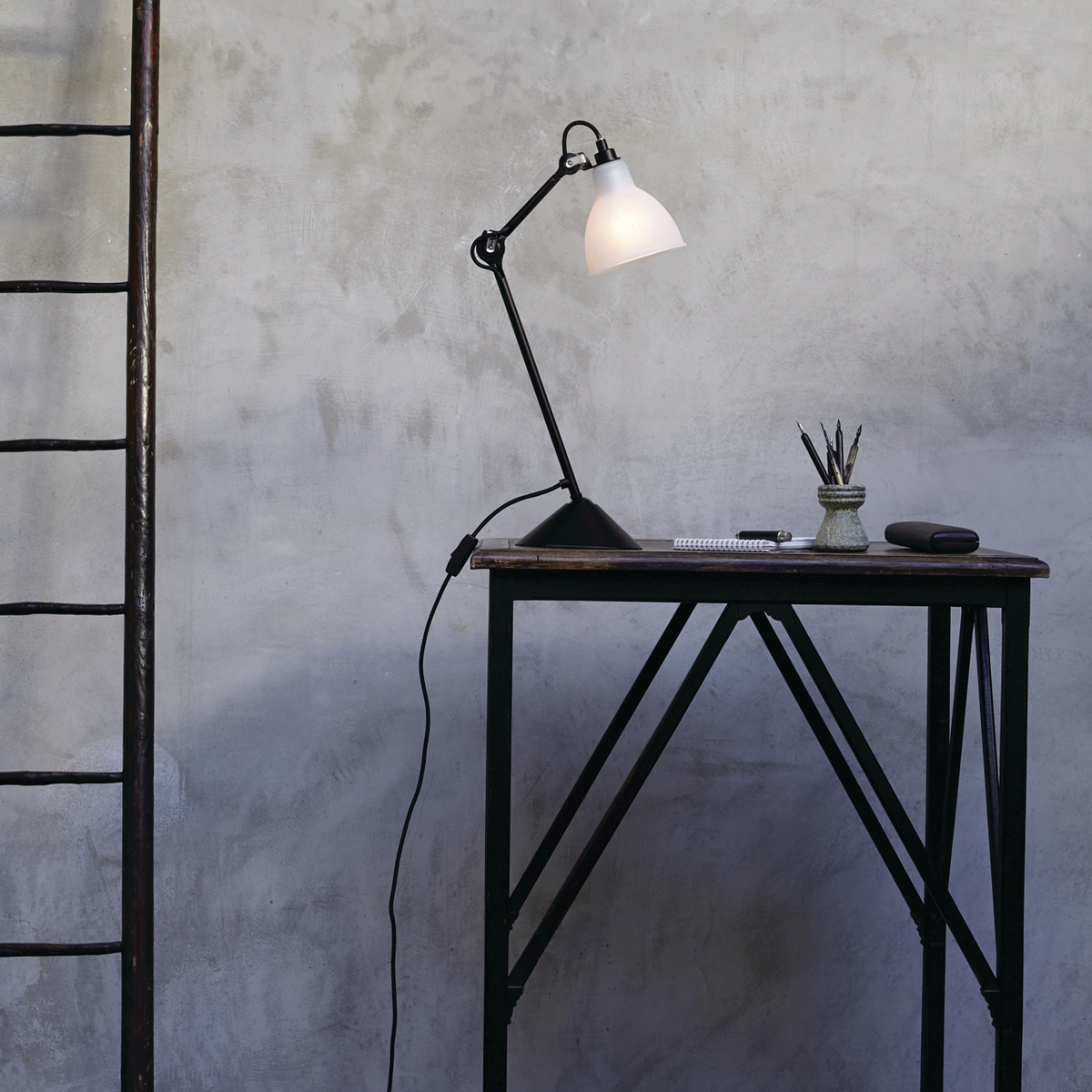 Black desk lamp on small wooden desk against grey concrete background.