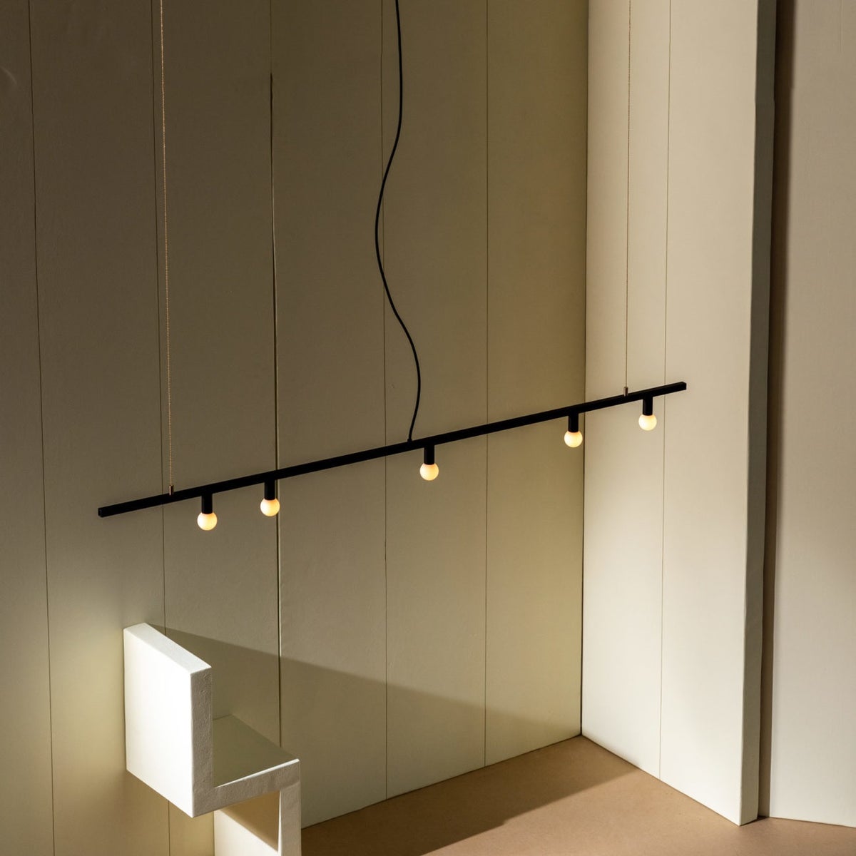 Black linear light with five lit bulbs against a beige background