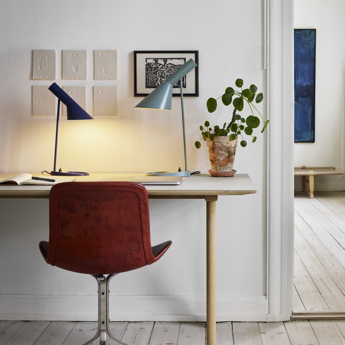 Two lit, angular desk lamps, one aqua and one navy, on white desk with plant.